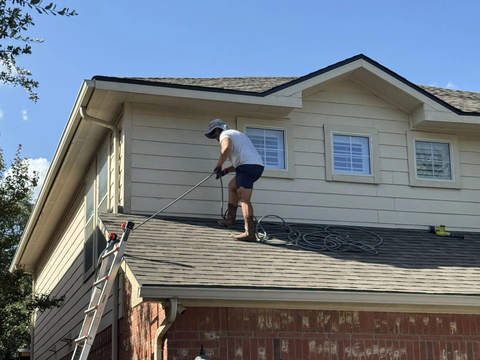 Technician on the roof of a two story home flushing the gutter with a wand