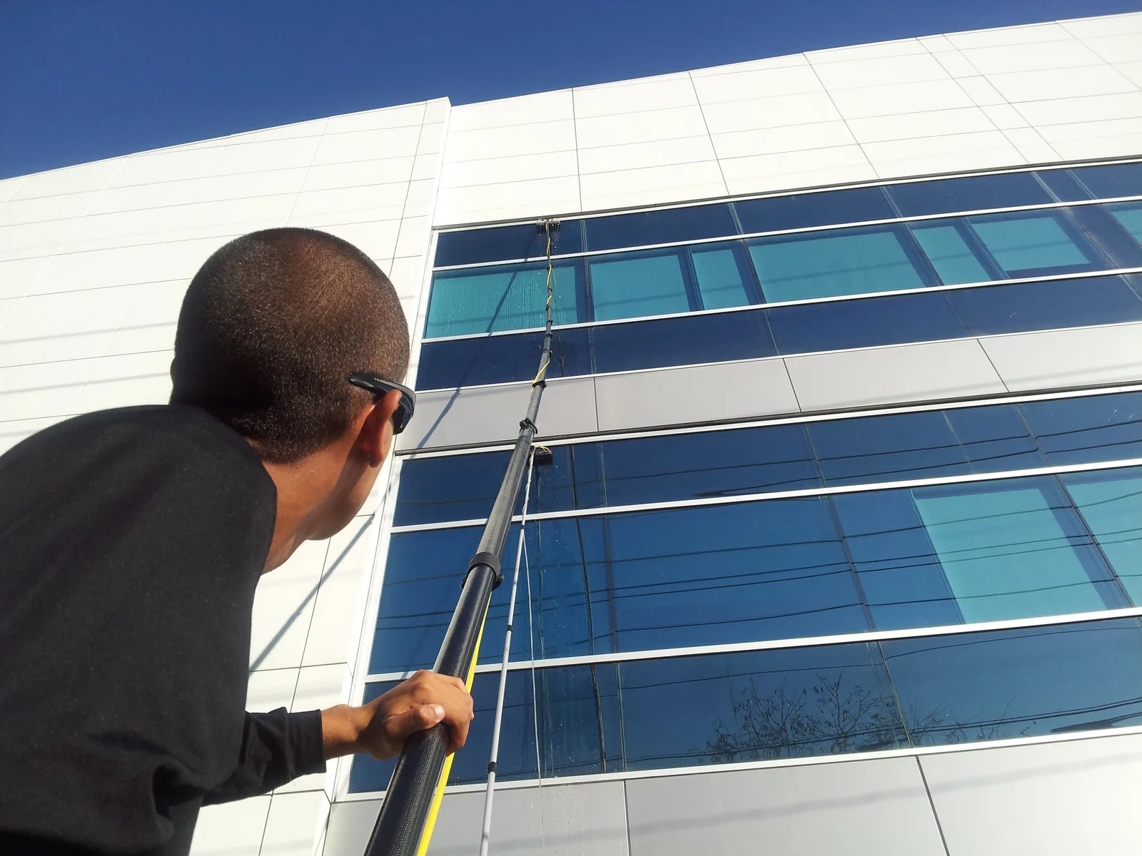 Technician washing office building windows from the ground with an extension pole