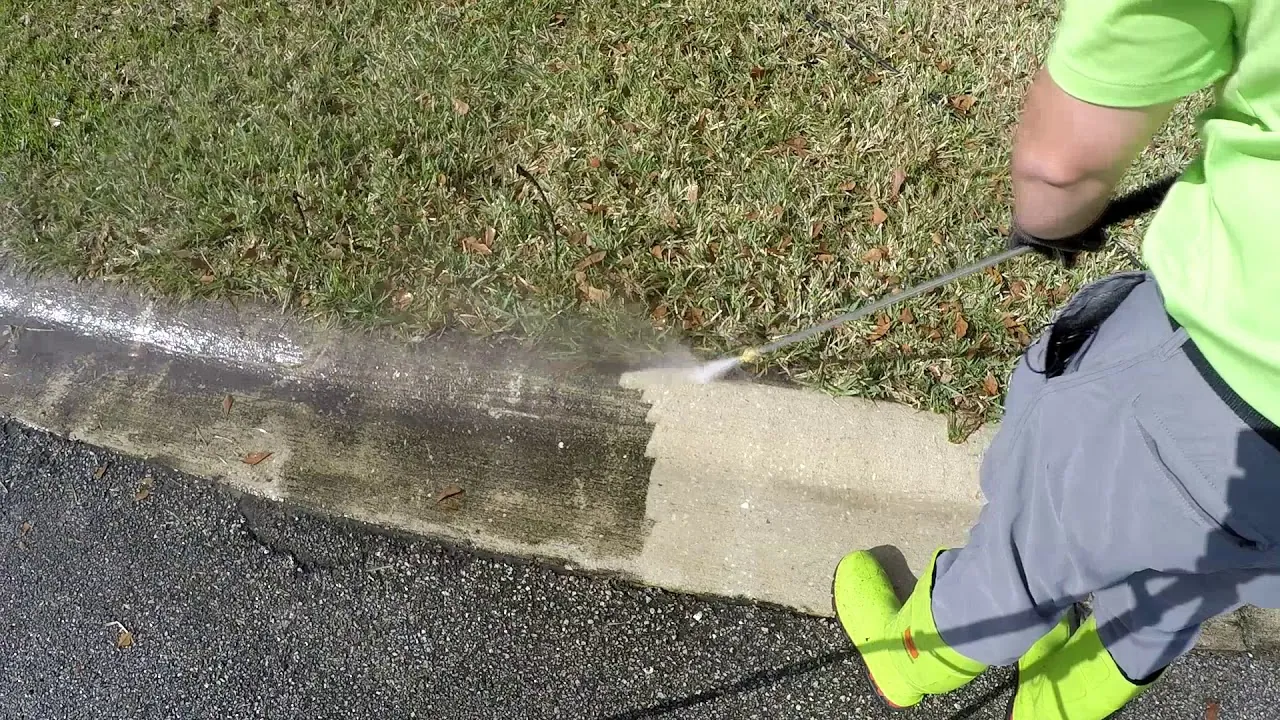 Concrete curb along a parking lot being pressure washed, half cleaned
