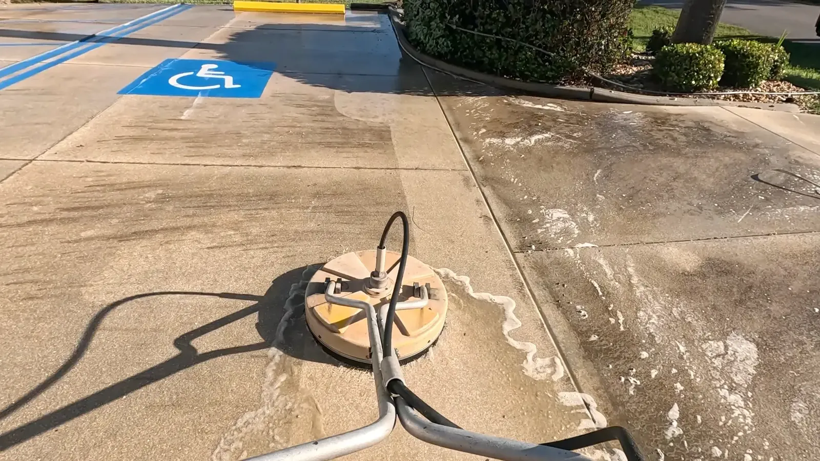 Surface cleaner pressure washing a concrete parking lot beside an accessible parking space