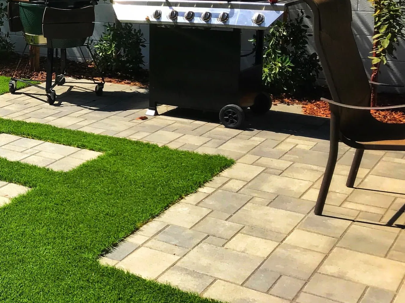 Paver patio laid beside an artificial turf lawn in a backyard