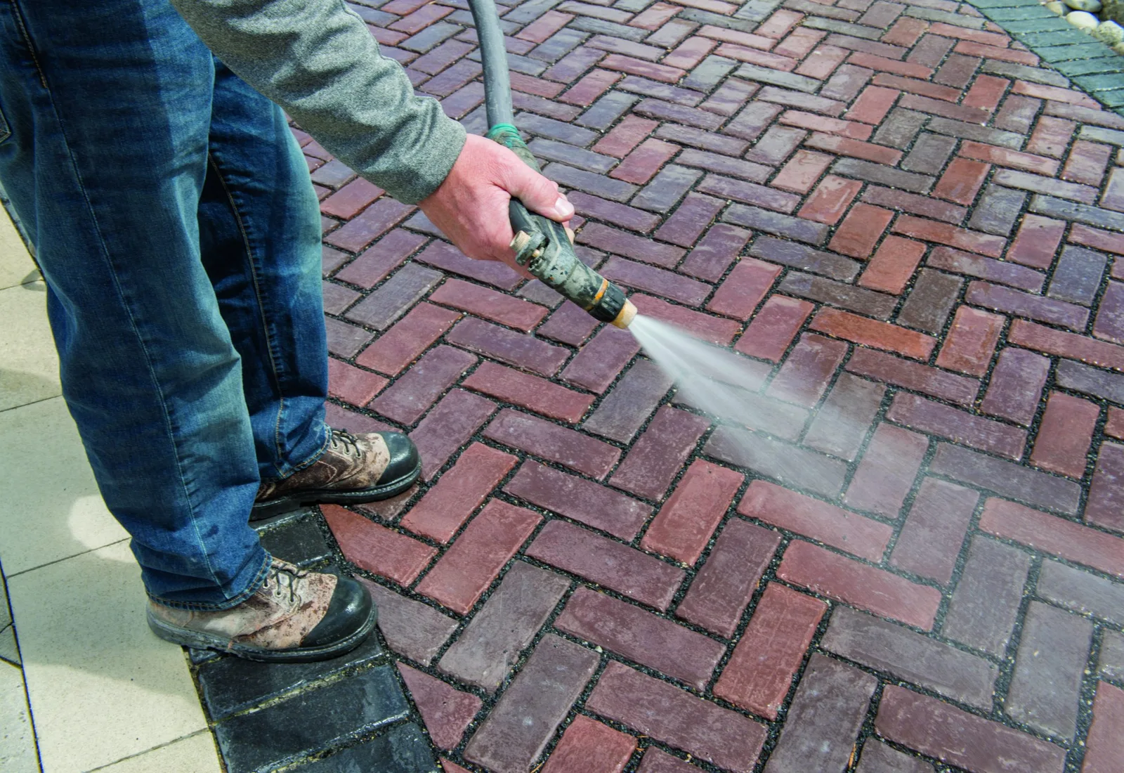 Close up of a brick paver patio being rinsed clean, one washed stripe next to the dirty pavers