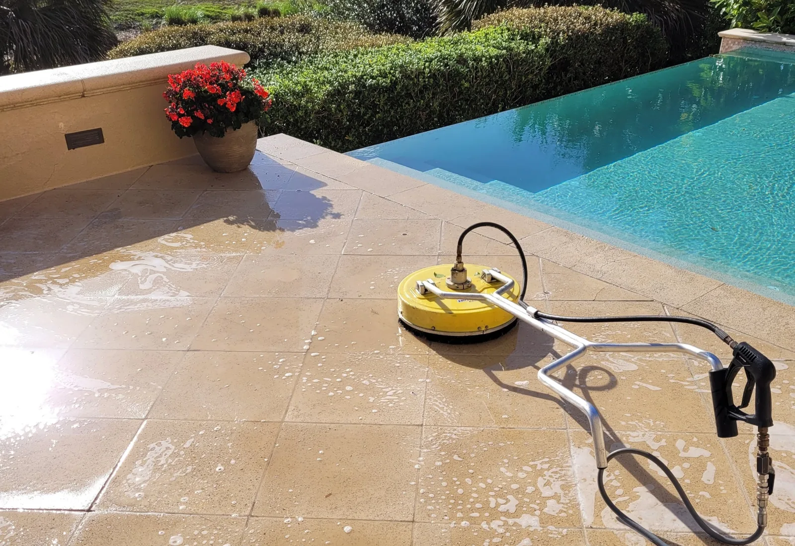 Surface cleaner attachment washing a travertine pool deck beside a backyard swimming pool