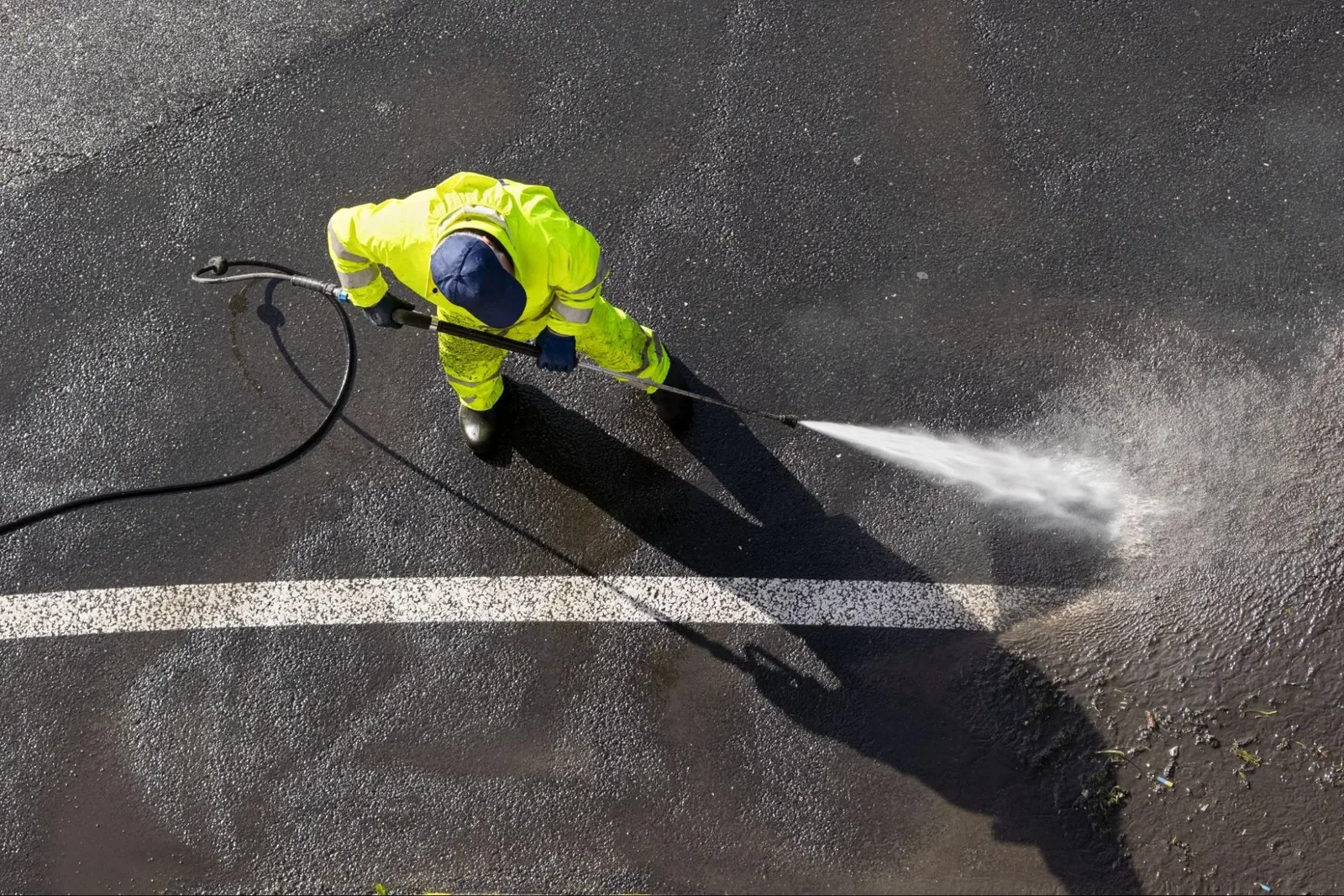 Pressure washer wand spraying dirty pavement leaving a clean stripe behind