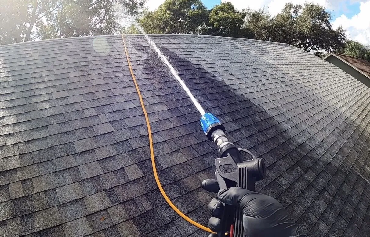 Low pressure soft wash spray running across an asphalt shingle roof during a roof cleaning