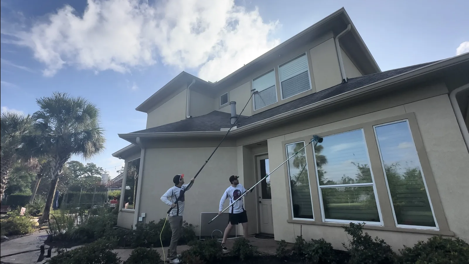 Technicians soft washing a two story stucco home with extension wands