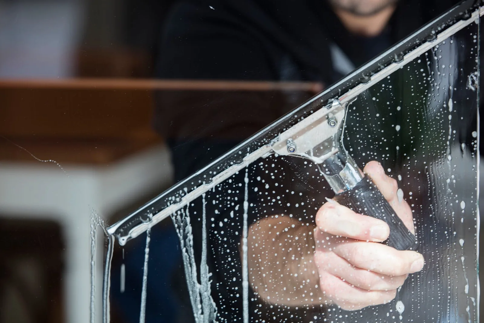 Close-up of a squeegee pulling soapy water down a storefront window pane