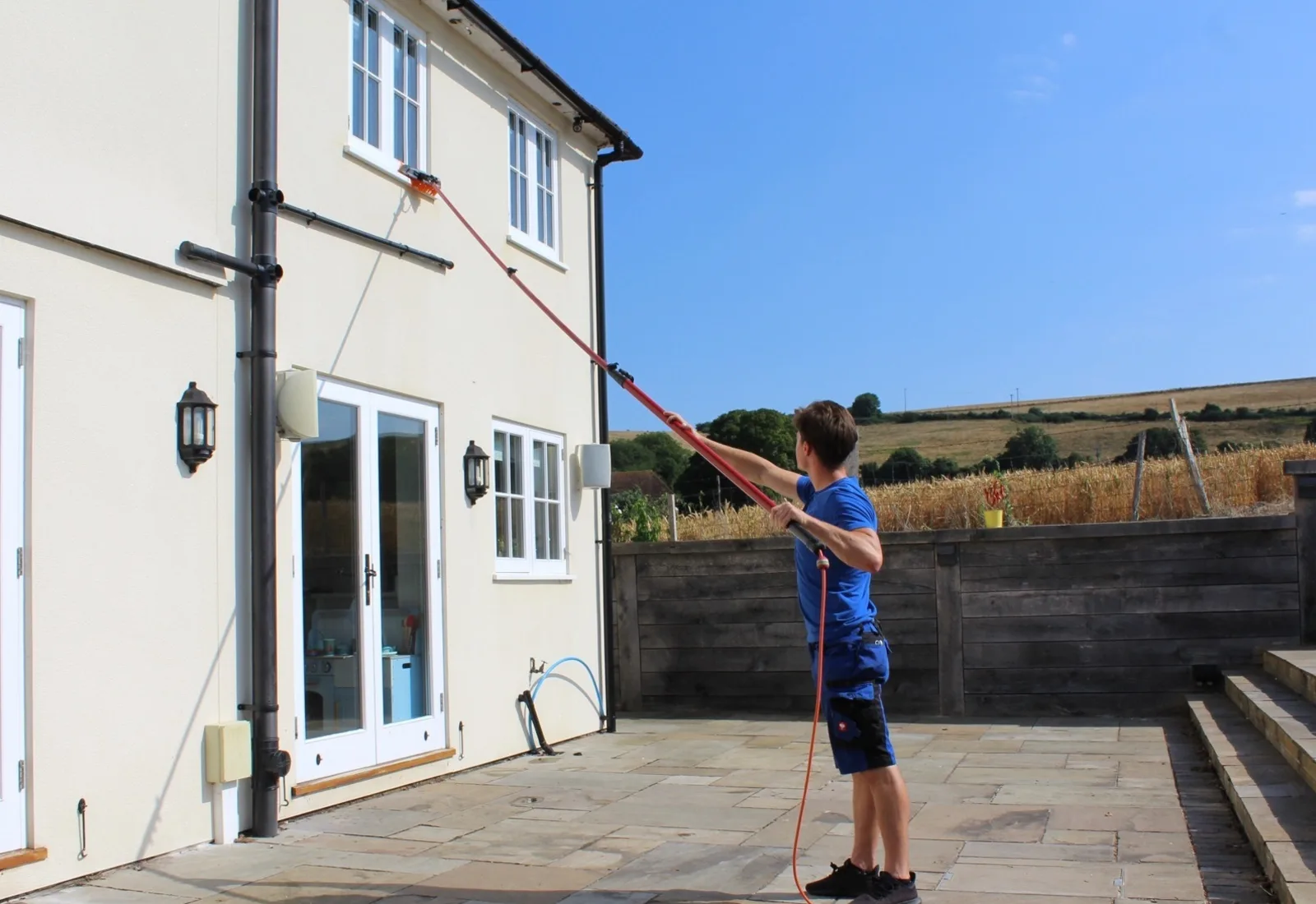 Window cleaning technician using a water fed pole to wash the upstairs windows of a house