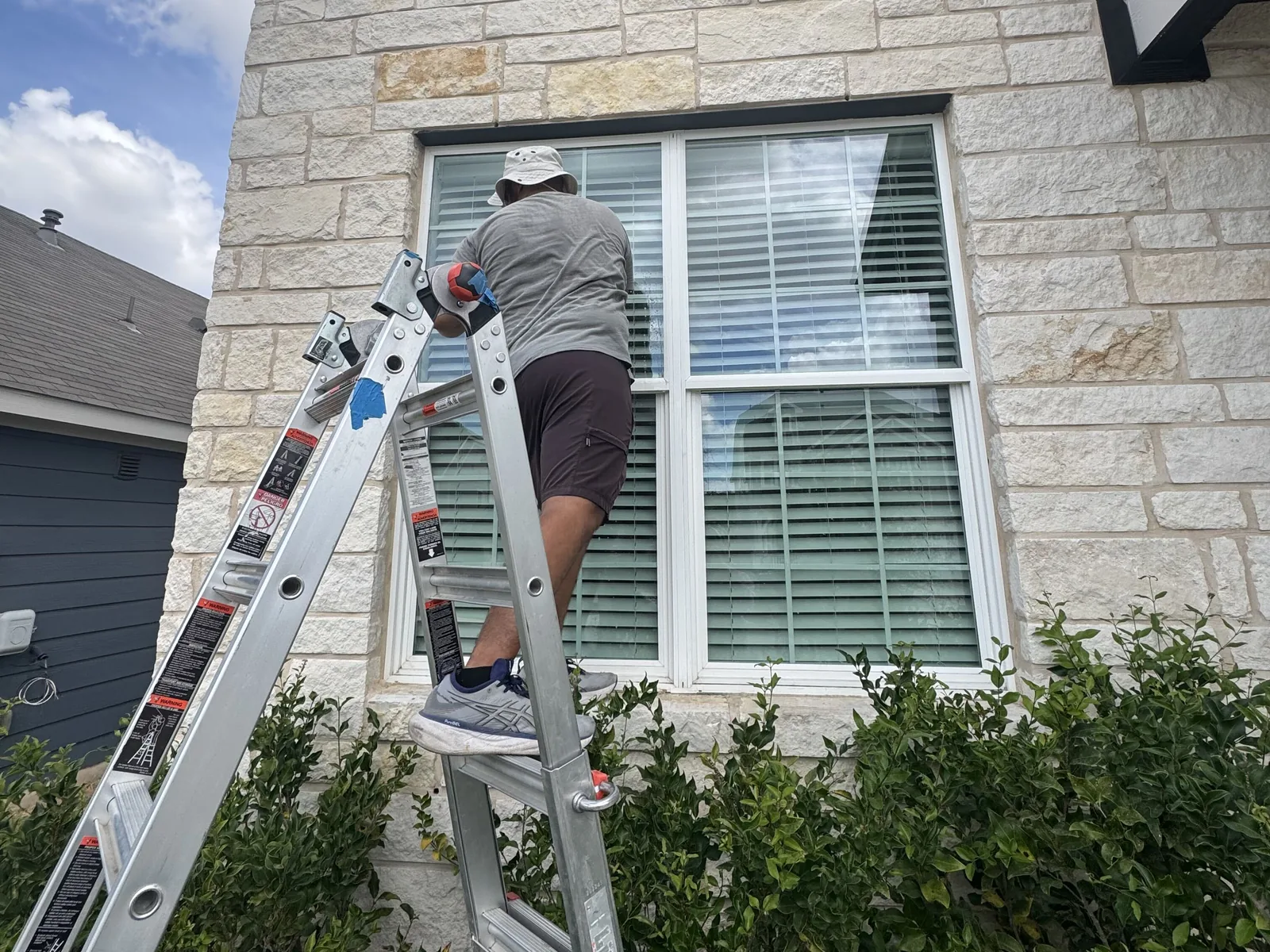 Technician on a ladder cleaning a double window on a stone home